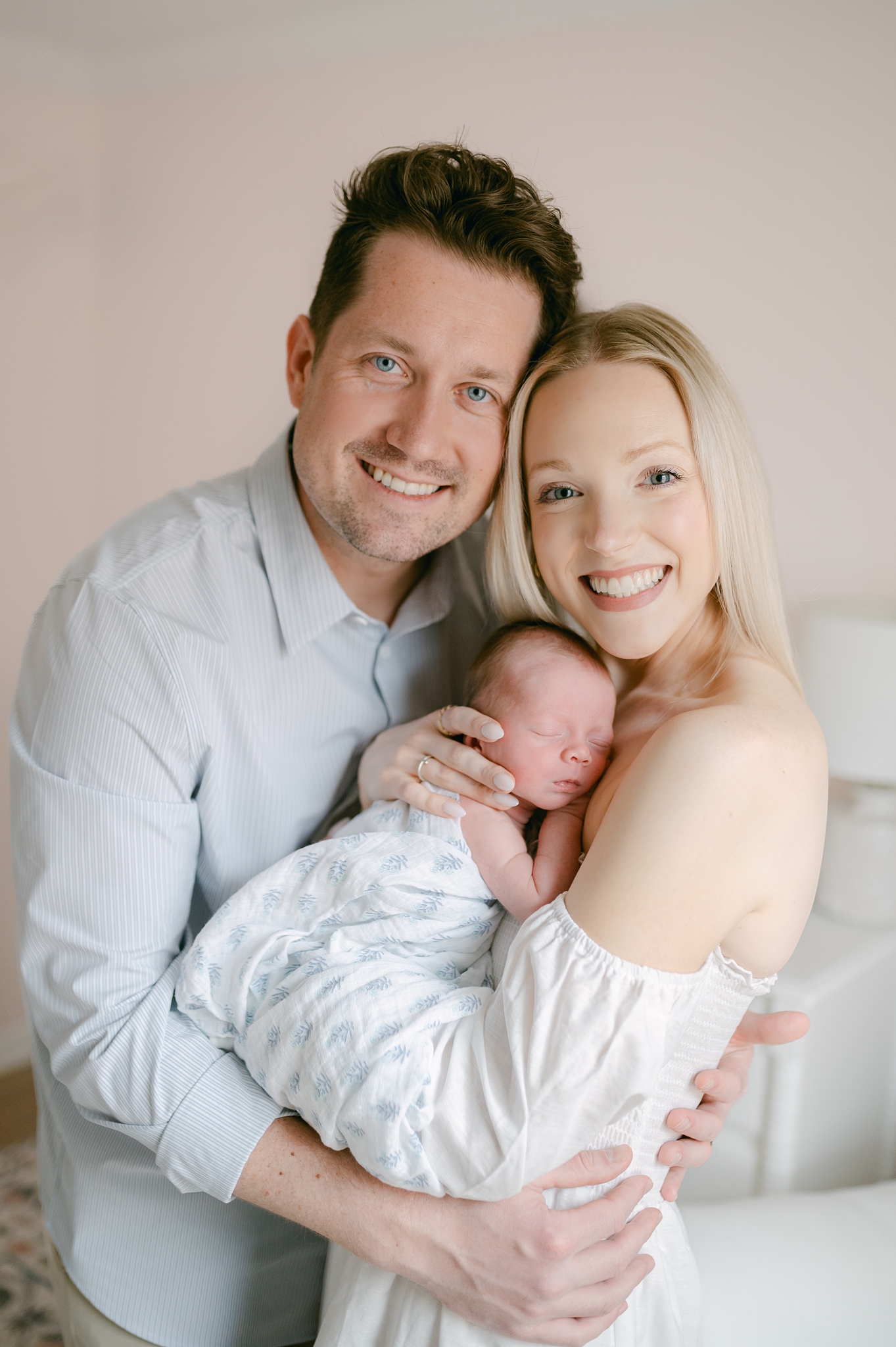 Mom, dad and newborn baby all smile at the camera during a photo session in Whitefish Bay.