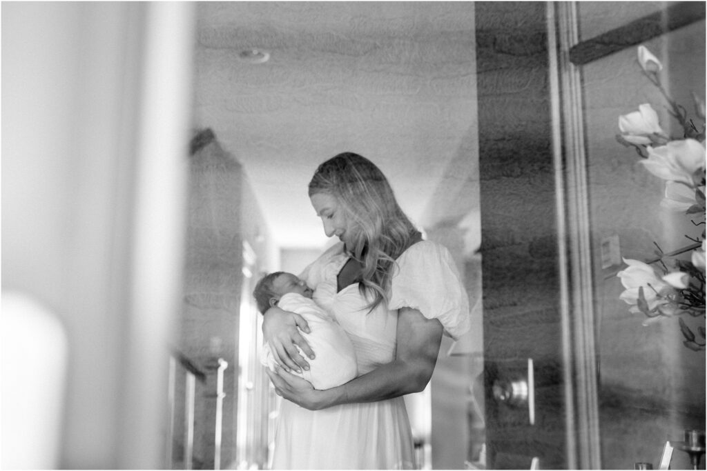 Black and white image of mom holding baby through the window during a newborn session.